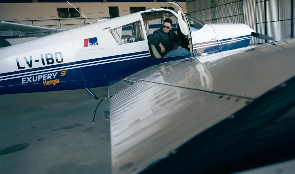 Pilot sitting in a Piper aircraft inside a hangar, ready for takeoff.